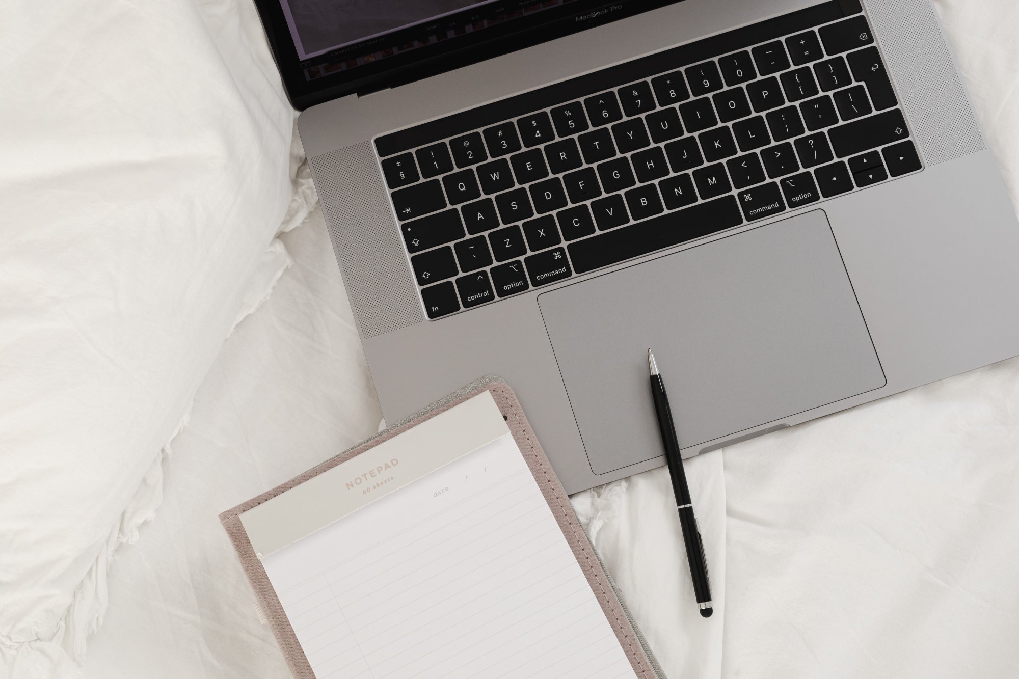 kaboompics_working-with-a-laptop-in-bed-white-cotton-bedding-blank-notebook-pen-28939.jpg
